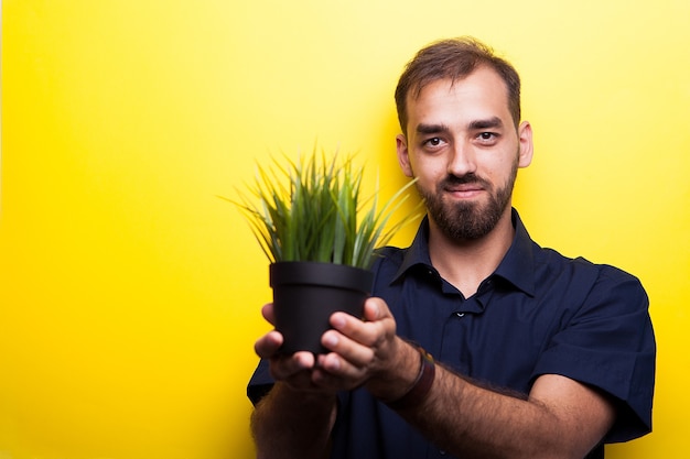 Sweet attractive young man showing a pot of grass on yellow background. ecology concept