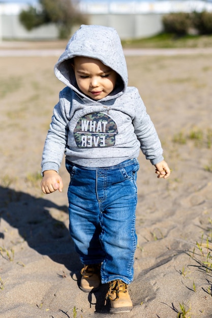 Dolce bambino in felpa con cappuccio e jeans che cammina e gioca nella sabbia attività con il bambino