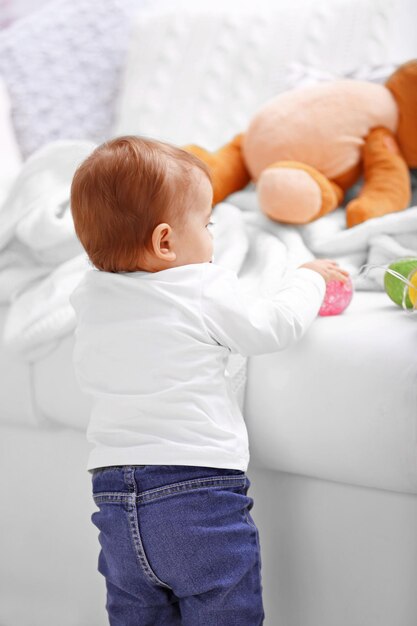 Photo sweet baby girl standing near the sofa