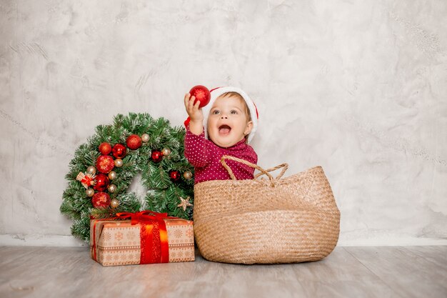 Sweet baby Santa sits in a wicker basket with a gift box