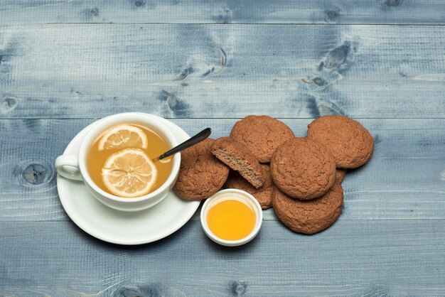 Sweet bakery and tea time Oatmeal biscuits as tasty pastry for cup of tea with lemon and honey Homemade dessert concept Cookies near tea on grey wooden background