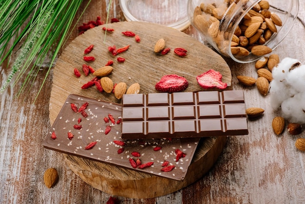 Sweet bar of chocolate with fruits and nuts on the wooden background