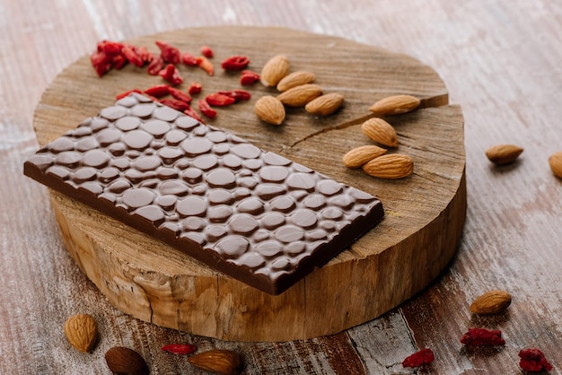 Sweet bar of chocolate with fruits and nuts on the wooden background