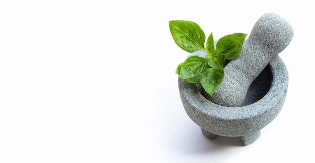 Sweet basil leaves in rock mortar with pestle on white