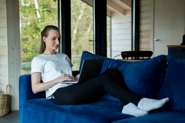 A sweet beautiful woman works at a laptop sits on the sofa at home check online stores for cyber mon