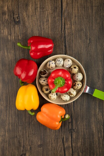 Sweet bell peppers and pan of quail eggs on wooden surface