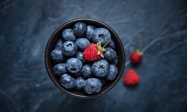 Sweet  blueberry in  bowl with raspberry  on dark background