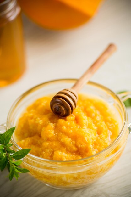 Sweet boiled pumpkin porridge in a bowl with honey on a light wooden table