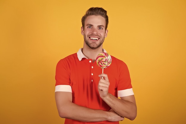 Sweet boy Symbol of happiness Man eat lollipop Man smiling hold lollipop Holiday concept Sugar harmful for health Guy lollipop candy yellow background Taste of childhood Happy eating sweets