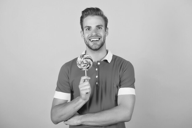 Sweet boy Symbol of happiness Man eat lollipop Man smiling hold lollipop Holiday concept Sugar harmful for health Guy lollipop candy yellow background Taste of childhood Happy eating sweets