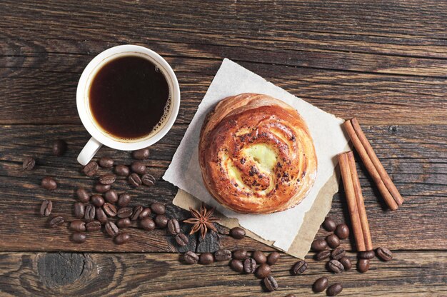 Sweet bun and cup of coffee on dark wooden table