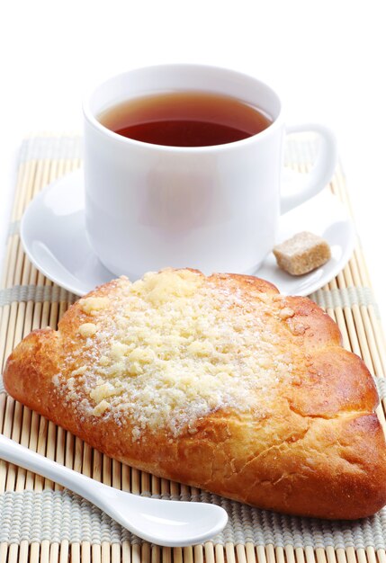 Sweet bun and cup of tea on white table