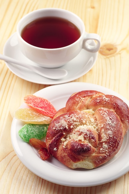 Sweet bun and cup of tea with dried fruit on wooden table