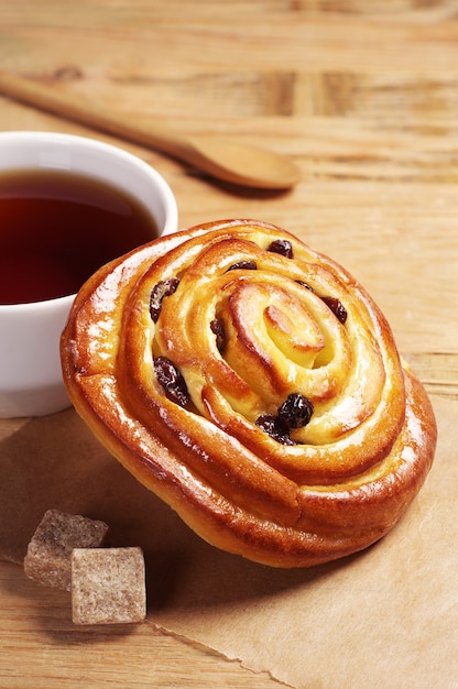 Sweet bun with cup of tea on old wooden background