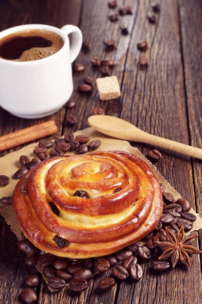 Sweet bun with raisins and cup of hot coffee on dark wooden table