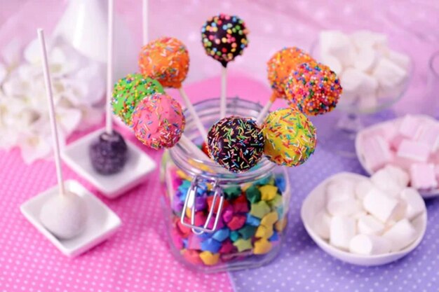 Sweet cake pops in jar on table on bright background