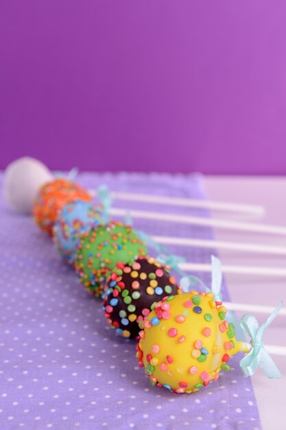 Photo sweet cake pops on table on purple background