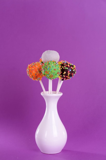 Sweet cake pops in vase on purple background