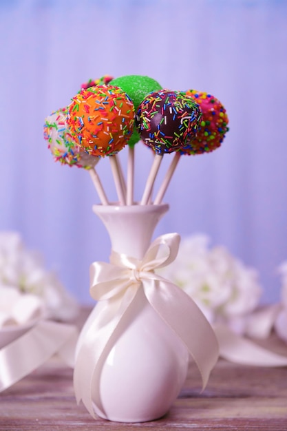 Sweet cake pops in vase on table on light background