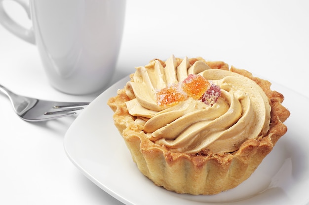 Sweet cake with cream in a plate and white cup