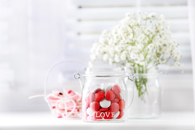 Sweet candies in jar with flowers on windowsill background