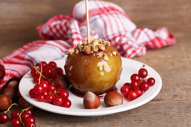 Sweet caramel apple on stick with berries, on wooden table