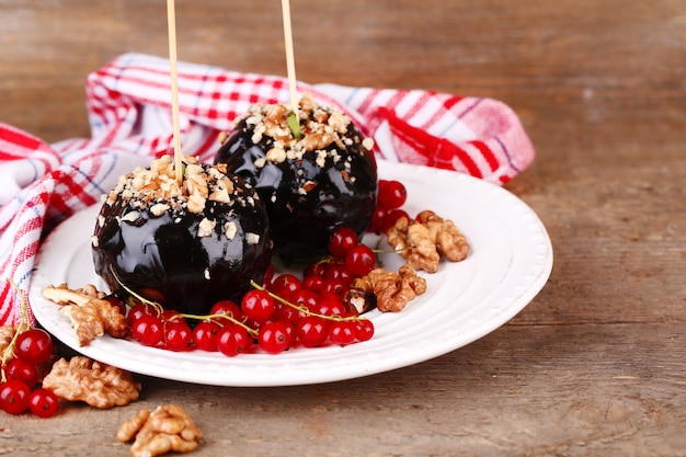 Sweet caramel apples on sticks with berries, on wooden table