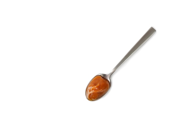 Sweet caramel sauce in spoon isolated on white background Melted liquid toffee Top view