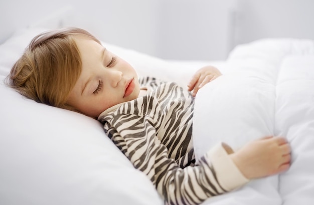 Sweet caucasian blonde adorable cute baby girl toddler sleeping in bed on white sheets under warm bl