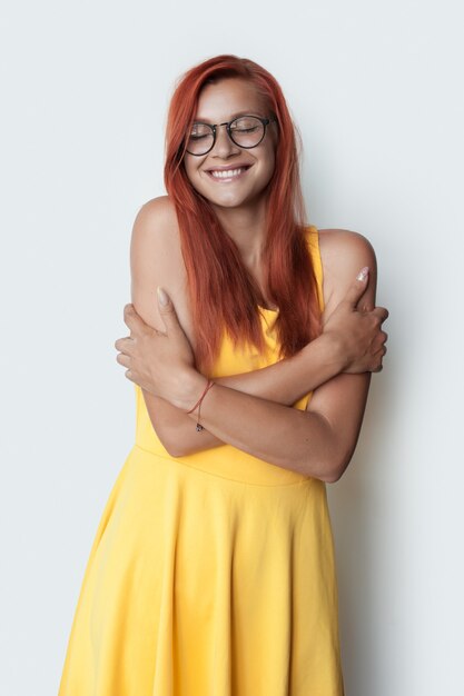 sweet caucasian ginger lady embracing herself wearing a yellow dress on white  wall