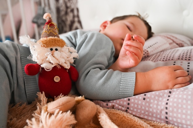 Sweet caucasian toodler boy sleeping in his bed with a toy gnome