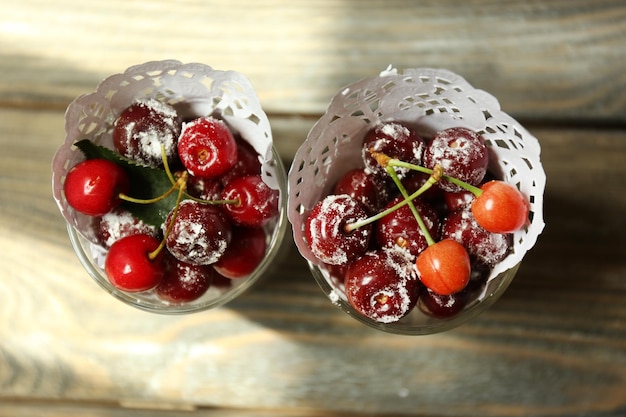Sweet cherries in glasses on wooden table