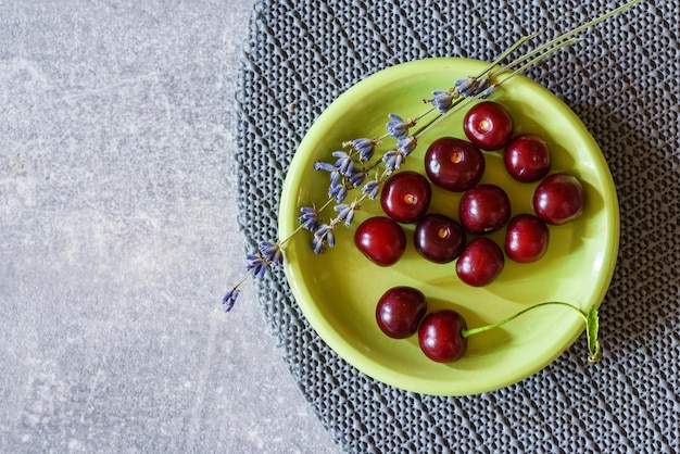 회색 대리석 테이블에 있는 녹색 접시에 달콤한 체리와 라벤더 꽃
