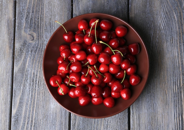 Sweet cherries on plate on wooden background