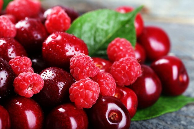 Sweet cherries raspberries with green leaves on wooden background