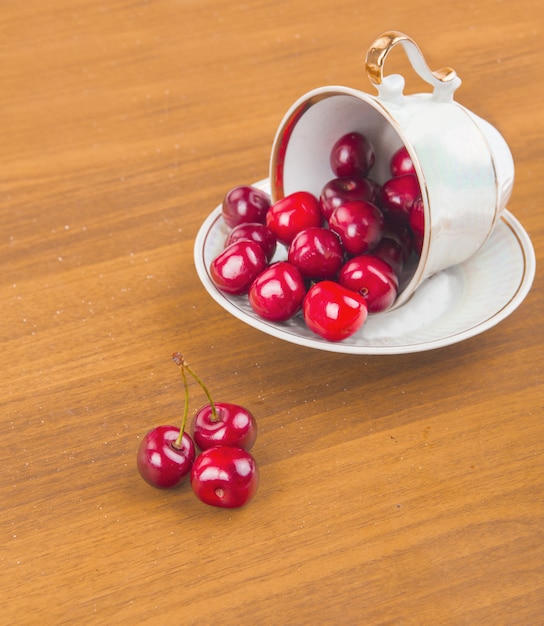 Sweet cherries in a white cup on a wooden table with two cherries in the front