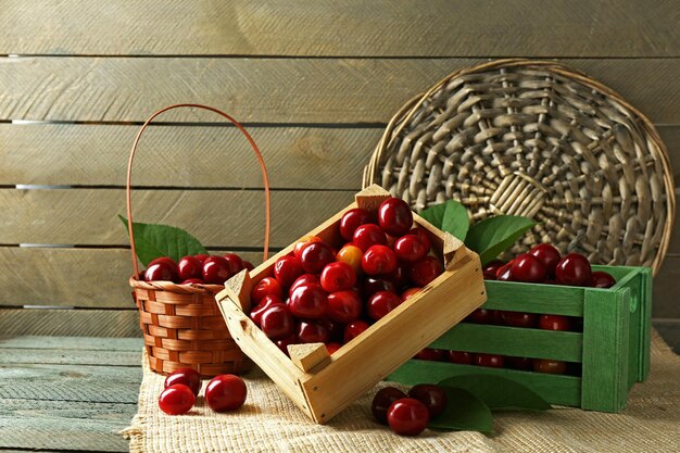 Sweet cherries with green leaves in basket and wooden boxes on wooden background