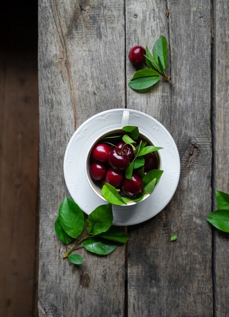 Sweet cherries with leaves in a white tea cup on wooden table