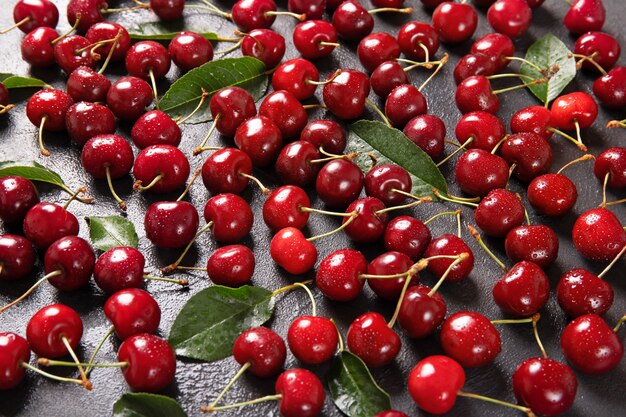 Photo sweet cherry on a black background with leaves and drops of water. view from above