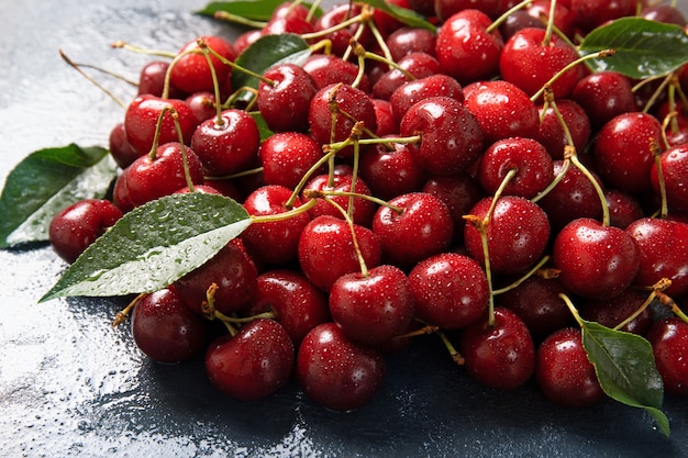 Sweet cherry on a black background with leaves and drops of water.