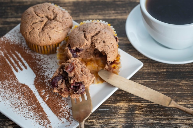 Sweet cherry muffin and white cup with tea on a wooden background