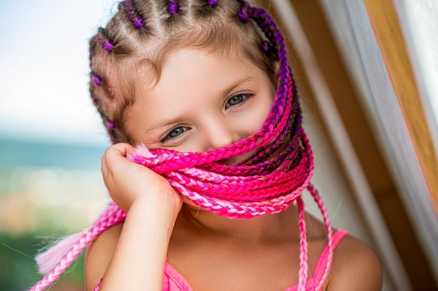 Sweet child girl with pinkred afropigtails dreadlocks Child in bright pinkred Little girl hairstyle from African braids Small girl pink afropigtails