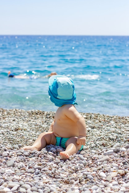 Sweet chubby baby on a pebble beach. Blue sea and summer sunshine