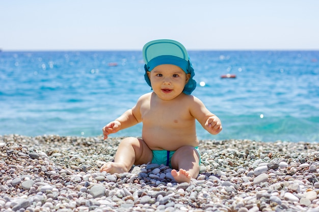 Sweet chubby baby on a pebble beach. Blue sea and summer sunshine