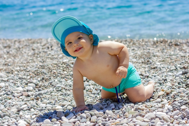 Sweet chubby baby on a pebble beach. Blue sea and summer sunshine