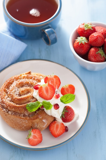 Sweet cinnamon roll with cream and strawberry for breakfast