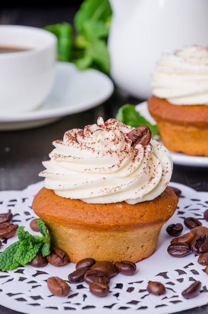 Sweet coffee cupcakes with butter cream and grains of coffee on a dark wooden background