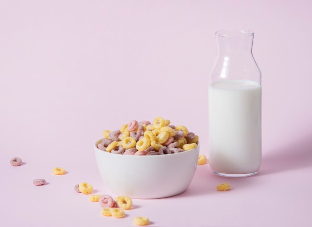 Photo sweet colorful cornflakes rings in a white bowl with a bottle of milk on a pink background. front view and copy space image