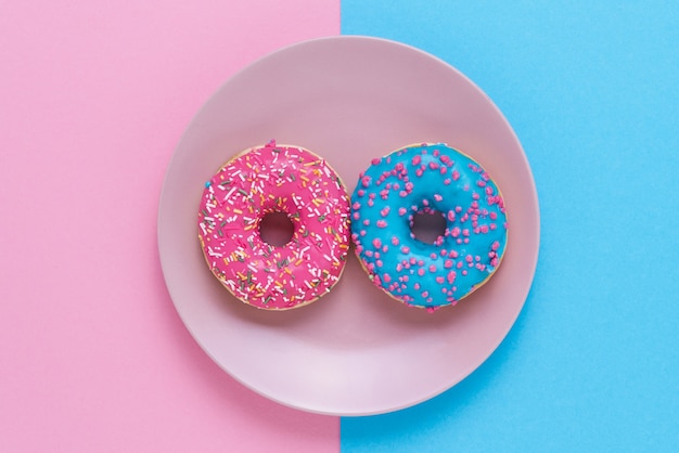 Sweet and colourful doughnuts on the plate on pink-blue backdrop. Top view, copy space.