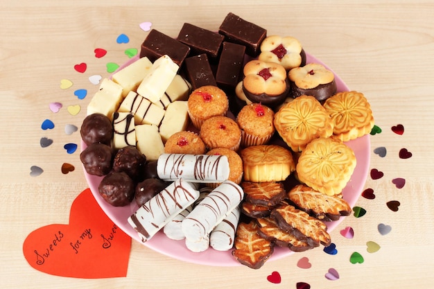 Sweet cookies with valentine card on plate on wooden background